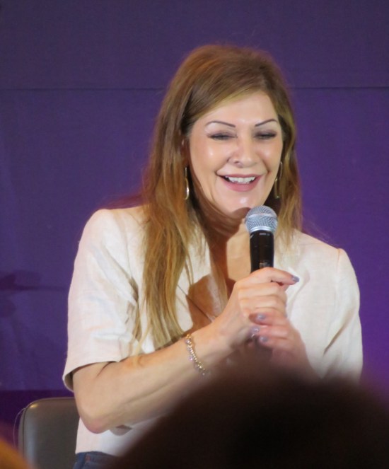 Marina Sirtis smiling onstage with mic.