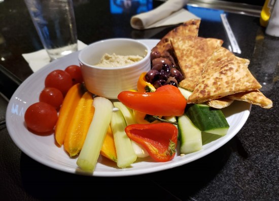 Plate with two kinds of olives, three kinds of peppers, cherry tomatoes, cucumber, celery, hummus and pita wedges.