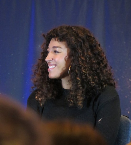 Tawny Newsome sitting on stage, turned and smiling.