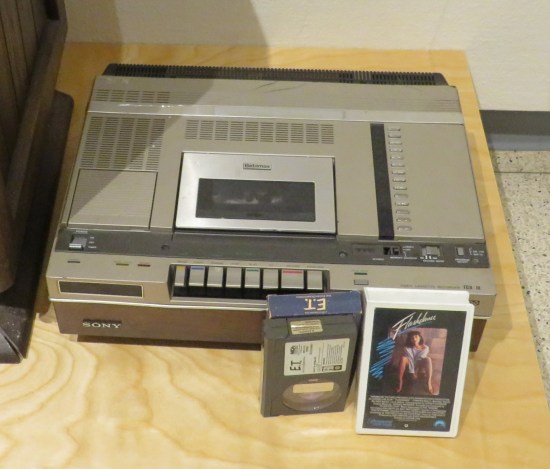 An old VCR with copies of "Flashdance" and "E.T." standing next to it.