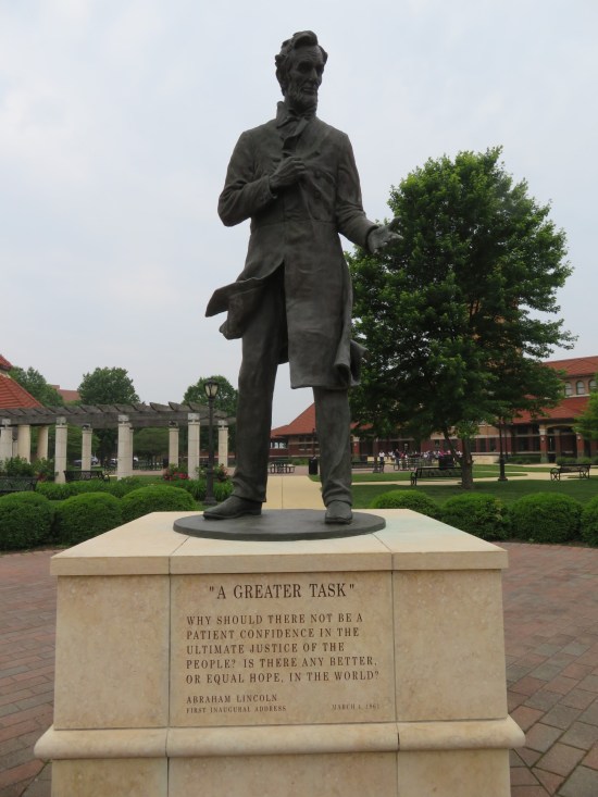 Outdoor bronze statue of President Lincoln in an overcoat giving his farewell address on a concrete pedestal.