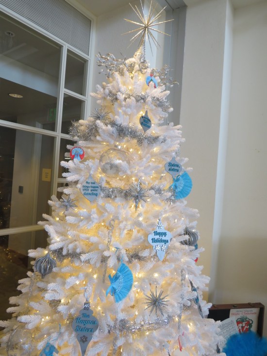 White Christmas tree decorated with ornament-shaped cutouts naming upcoming productions.