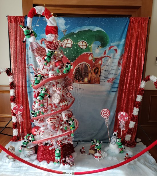White Christmas tree with red track spiraling around it and covered in tiny Chick-Fil-A cows in elf costumes pretending to decorate.