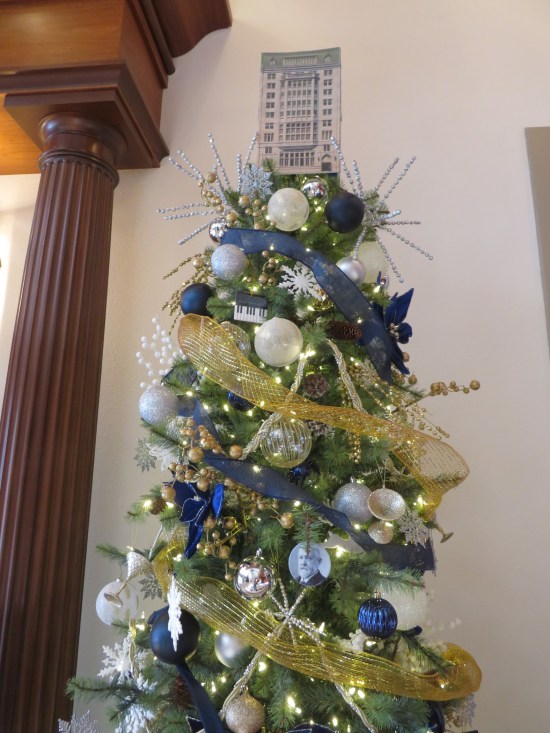 Christmas tree with blue and white balls, yellow netting, and a tree topper that's a model of a 10-story Gothic Revival building.