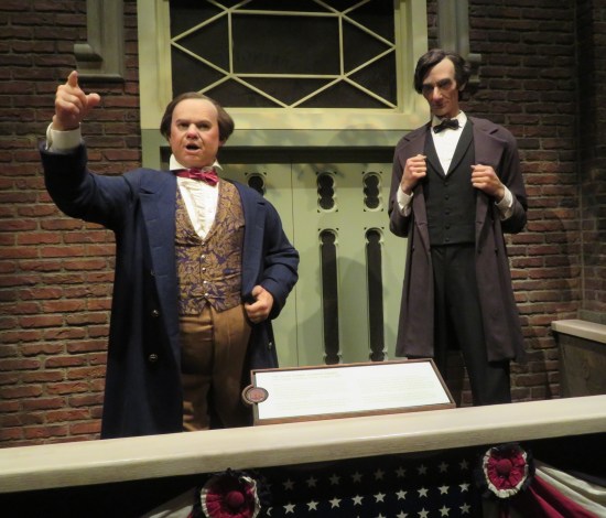Statues of Stephen Douglas and Abe Lincoln on a balcony. Douglas is speechifying, one fist raised and pointing a finger.