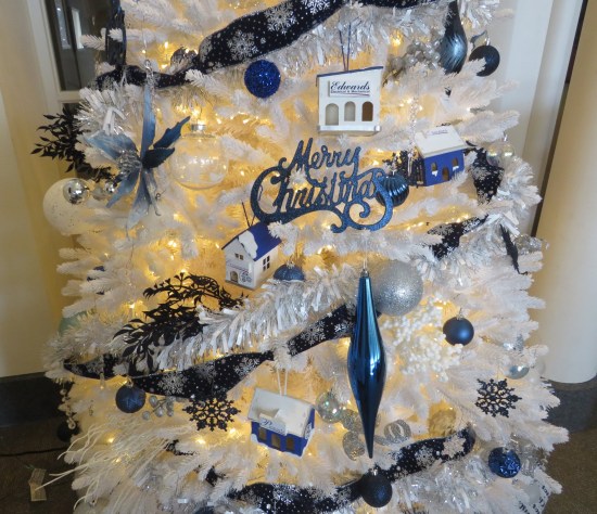 White Christmas tree decorated with all blue ornaments, including tiny store and the words Merry Christmas.