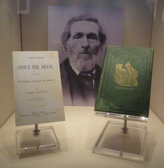 Two old books on stands in front of a photo of William Herndon. One called "A Few Words About the Devil" and a green hardcover called "Iconoclast".