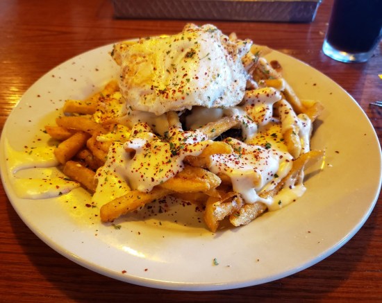 Plate with a mound of fries in cheese sauce and herbs, with a fried egg on top. 