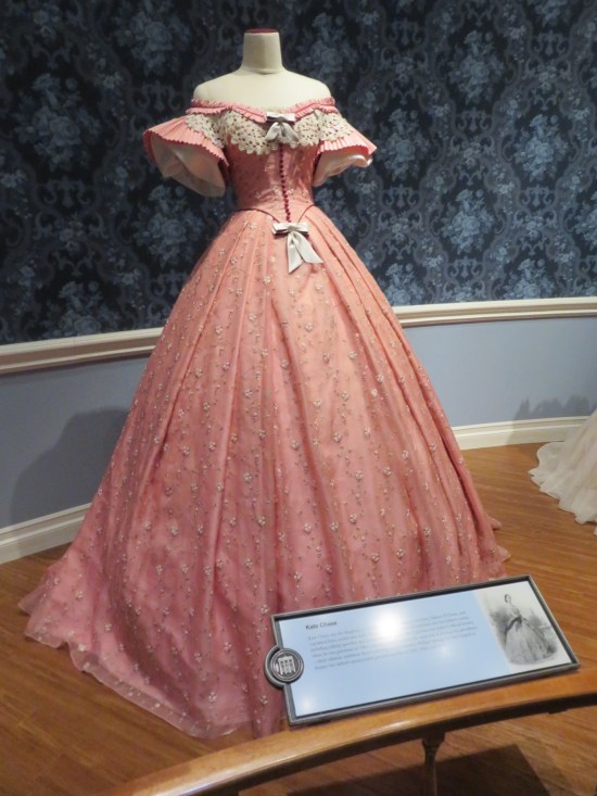 Pink ballroom dress, shoulders revealed, white bows on the bosom and belt. Bell-bottomed short sleeves.