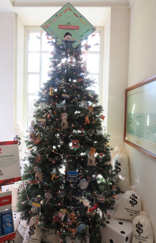 Christmas tree decorated with Monopoly stuff, including game board topper and money bags on the floor..