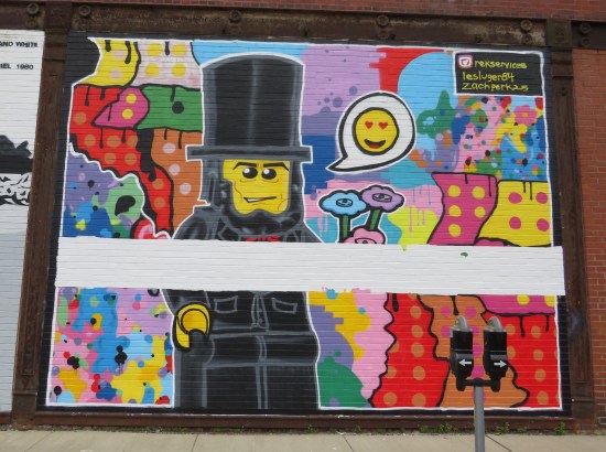 Mural of Lego Lincoln holding Lego flowers with a word balloon that's just a heart-eyed emoji.