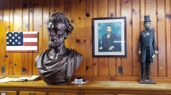 A Lincoln 8x10 painting, a foot-tall wood-carved Lincoln, and a Lincoln bust clad in Greco-Roman robe.
