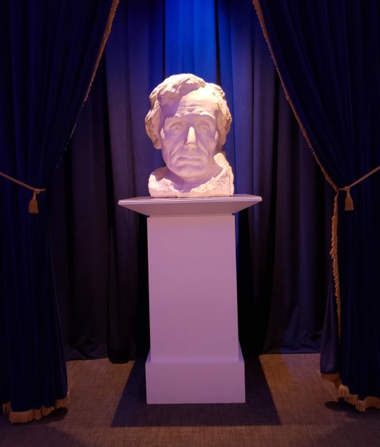 Lincoln bust on a pedestal, in a dark room but lit by purple spotlight.