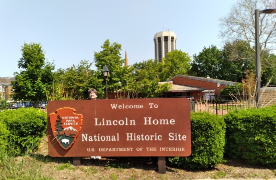 Large welcome sign for Lincoln Home National Historic Site with National Park Service emblem and Anne's head peeking over the top.