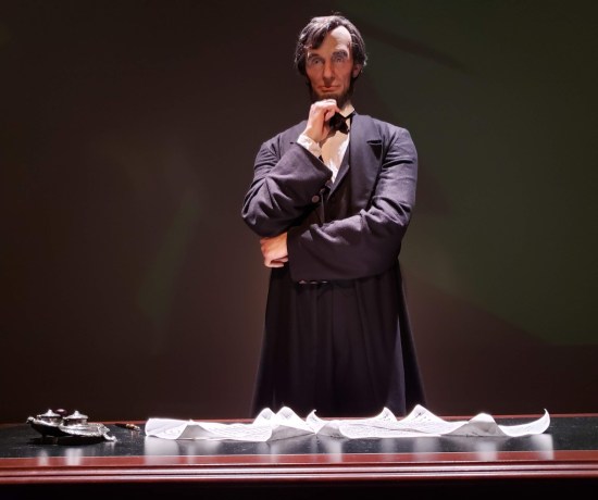 Statue of Lincoln pondering at a desk with parchments on it.
