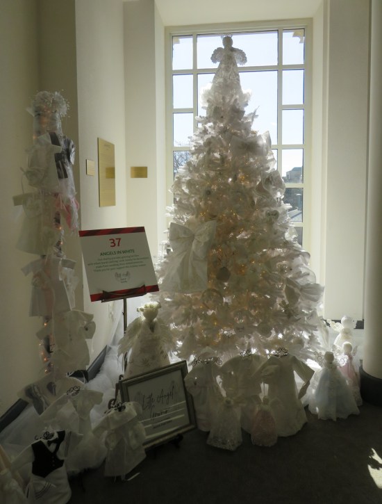 White Christmas tree decorated with angels and surrounded by same on the floor, each about 12-20 inches tall.