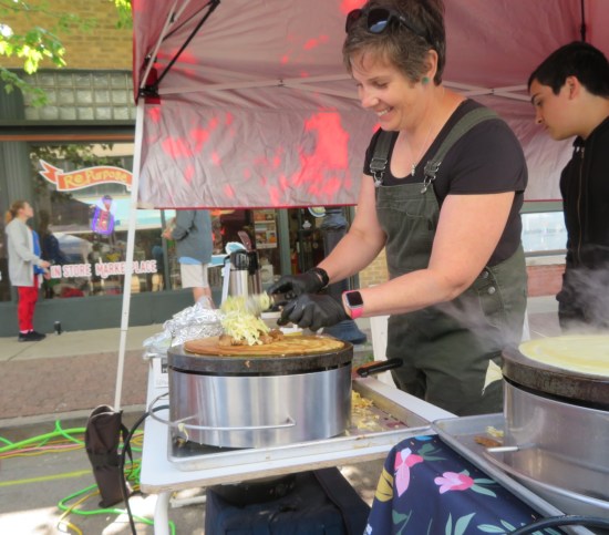 Nice lady making crepes on an electric griddle inside a pink tent.