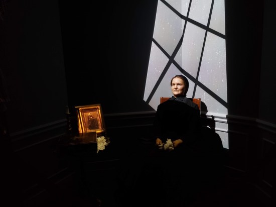 Statue of an older Mary Todd Lincoln sitting in the dark. Light pours into the shadow through a lone nine-pane window.