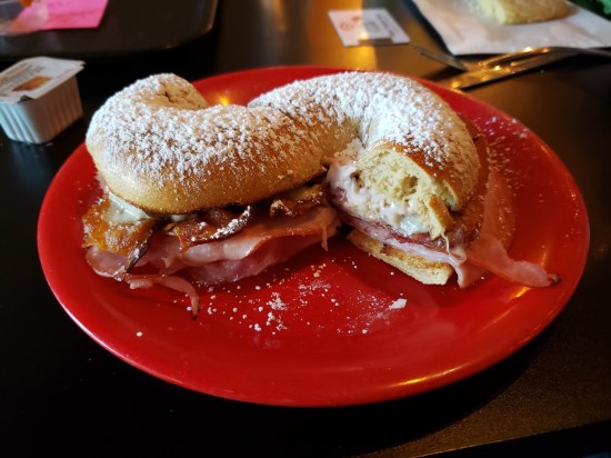 Bagel sandwich covered in powdered sugar, cut in half and served on a red plate.