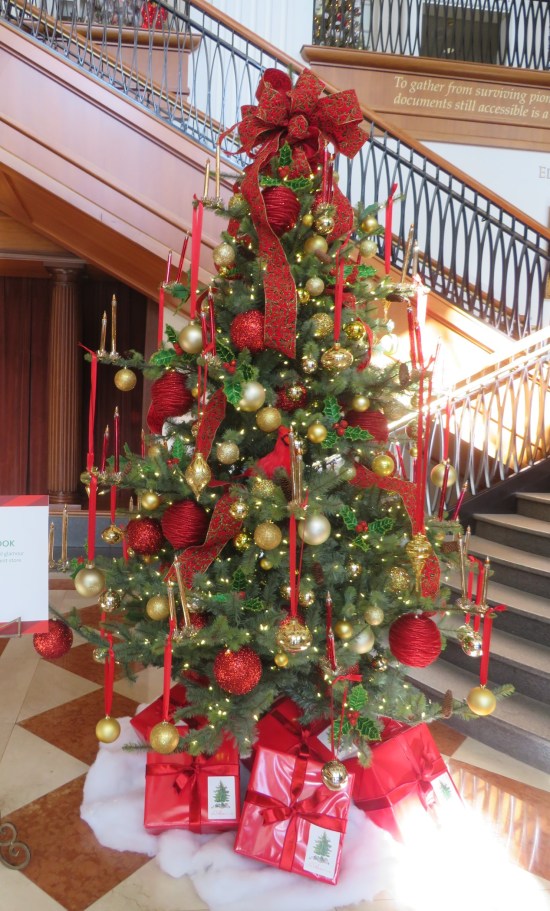 Christmas tree decorated with gold balls, red ribbons, tall candles, big red bow on top
