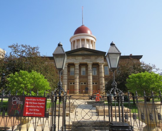 Old State Capitol locked front gate, with a sign thanking its keepers for letting them hold the Old Capitol Art Fair down the street out front.