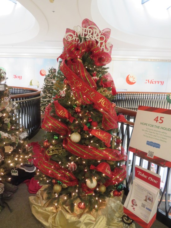 Christmas tree decorated with Merry Christmas topper, thick red ribbon reading Home for the Holidays.