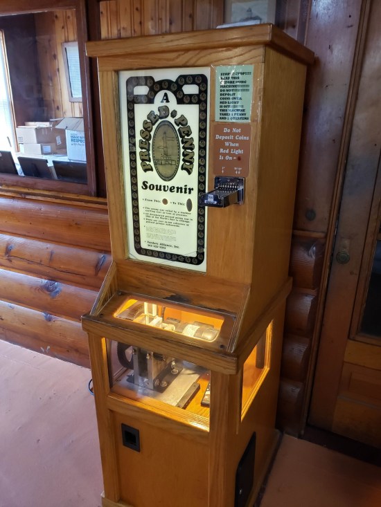 A smashed penny machine, all wood, in front of a wood wall.