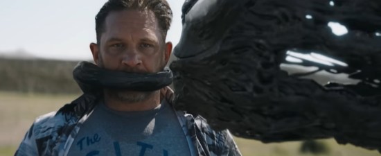 Tom Hardy in a desert with the symbiote still tethered to his back, but it's wrapped another tendril around his mouth to shut him up.