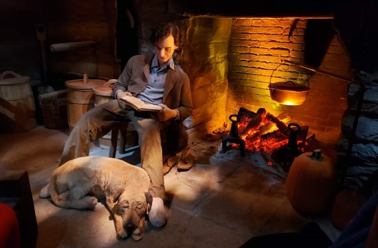 Statue of older teen Lincoln reading by a fireplace with a dog lying at his feet.