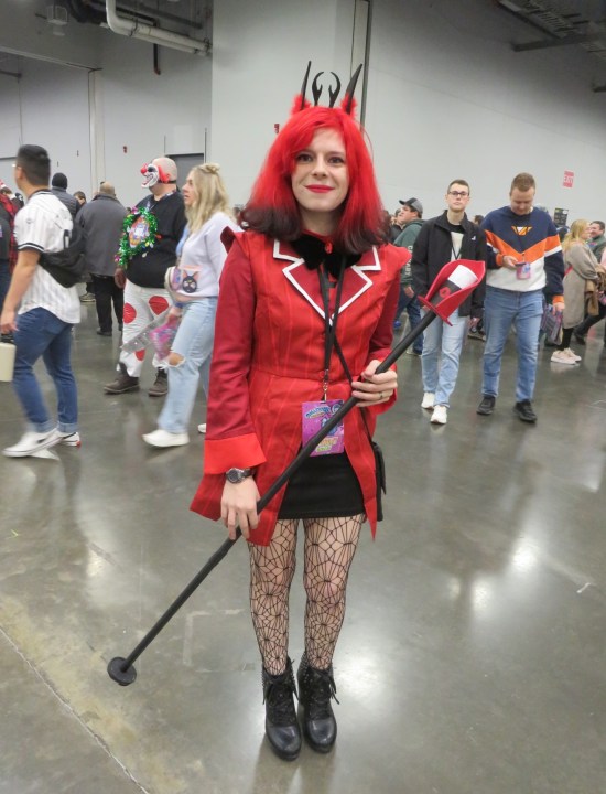 costume: red and black angular suit jacket, black skirt, spiderweb hose, and matching evil crown and cane with a mic on top.