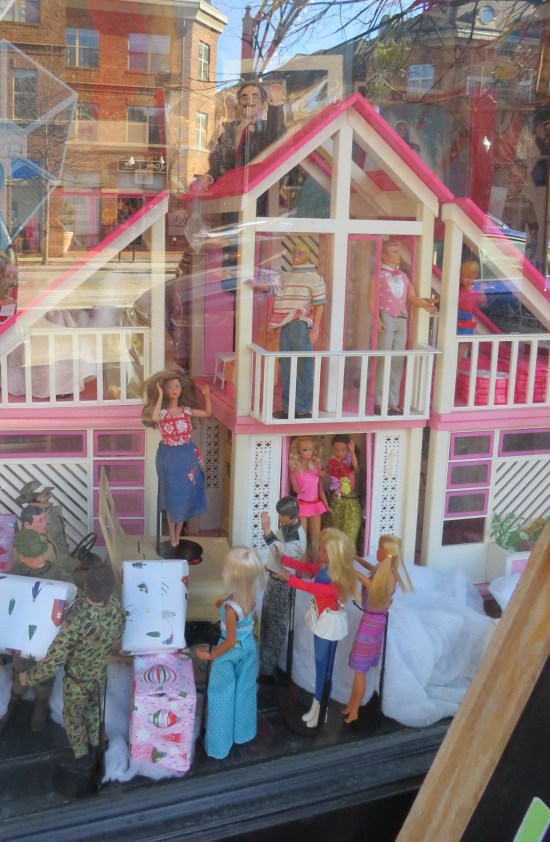 Barbie Dream House in a store window, surrounded by Barbies but with a Groucho Marx doll on top.