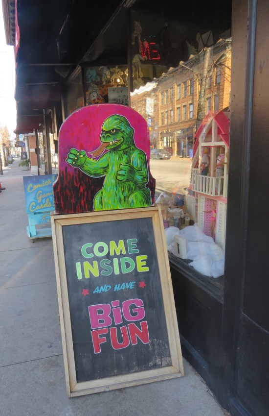 Folding sidewalk chalkboard reading "Come inside and have big fun." Drawing of Godzilla on top.