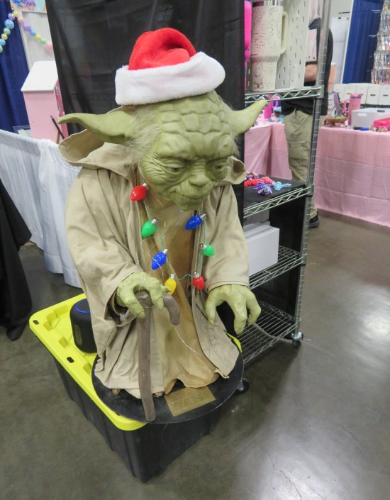 Life-size Yoda statue with cane, Santa hat and Christmas light strand around his neck.