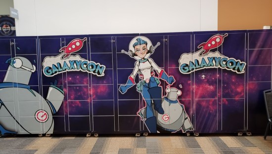 Six-foot backdrop of GalaxyCon logo, their space lady mascot, and nameless round robots.