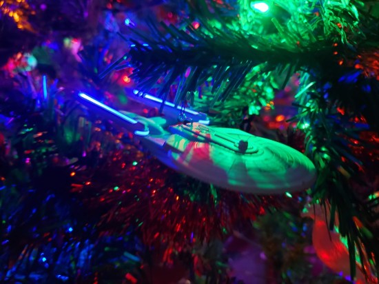 Star Trek Enterprise ornament with the blue nacelles lit up and other Christmas lights around it.