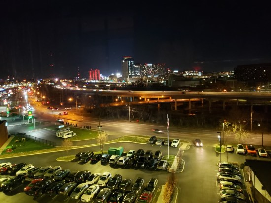 Nighttime view of a distant downtown across a brightly lit parking lot.