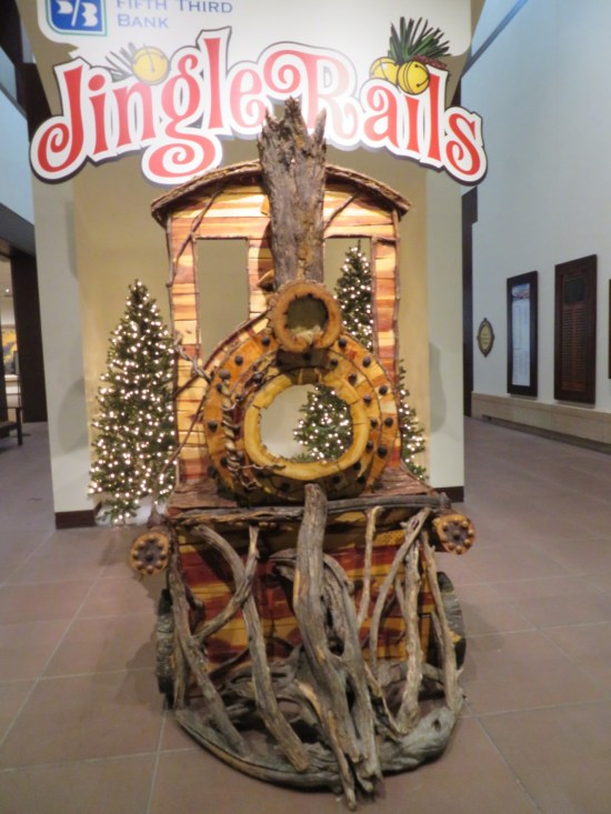 Train engine front car in a museum hallway, big enough for a child to drive if it worked. Jingle Rails logo hangs at the top of the wall behind it.