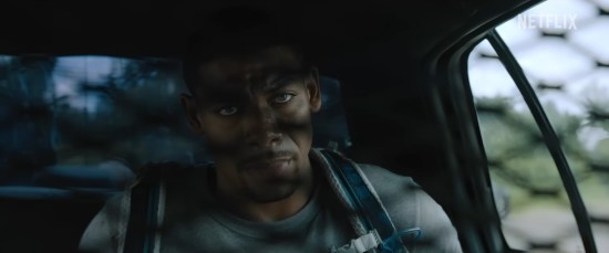 Black man sitting in the back of a police car, glaring through the divider. He SHALL overcome.