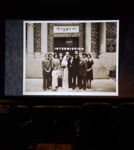 Sepia photo of the cast of "The Brutalist" dressed for pre-WWII in front of a Hebrew temple. It's projected on a movie screen, labeled "Intermission" and has a countdown clock that's at 11:07.