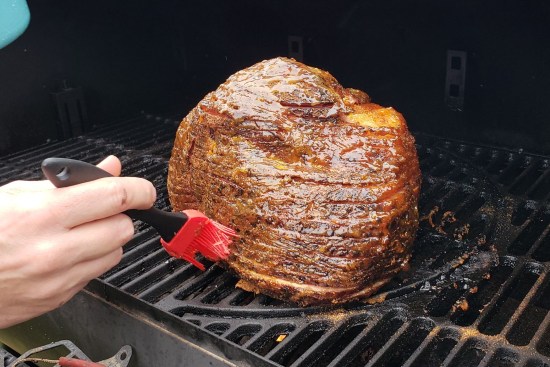 A Christmas ham cooking in an outdoor smoker. The chef is basting it.
