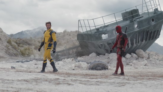Deadpool and Wolverine walk across a gray wasteland with half of a broken boat in the background.