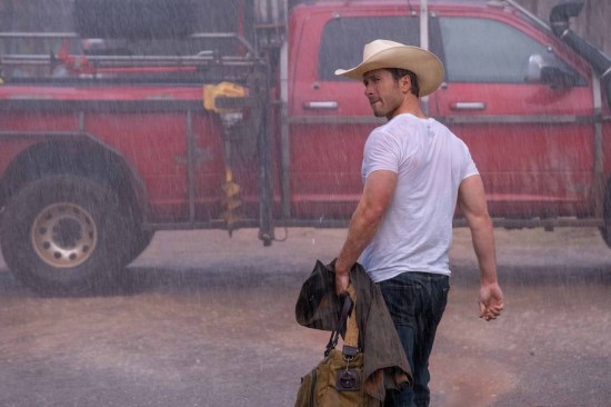 Glen Powell in a cowboy hat and white T-shirt, drenched in rain.