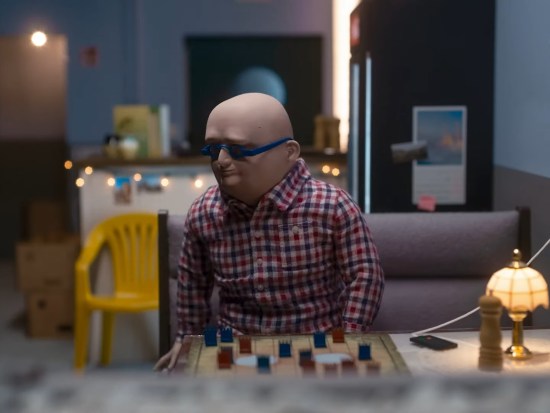 A stop-motion bald man arises from a table with a board game set up on it, something involving stacked tokens.