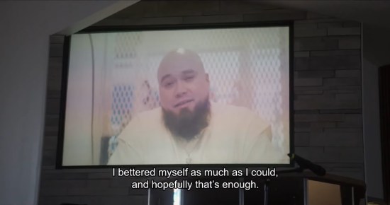 Video playing on a large TV at a funeral. On screen is the decedent, bald Latino man with beard. Subtitles: "I bettered myself as much as I could, and hopefully that's enough."