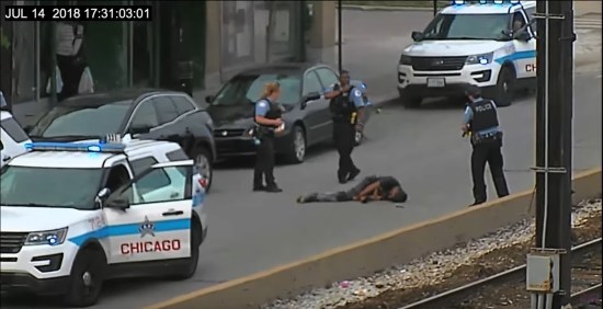 Grainy security cam footage of three police standing around a body in the middle of a Chicago street.