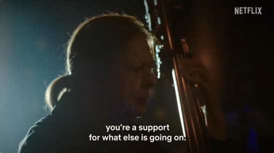 Very dark orchestra hall with our titular double bassist playing. Subtitles: "You're a support for what else is going on."
