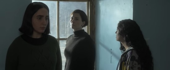 An Iranian mom stands at a window with her two daughters, one college age and one high schooler. Nobody's happy, everyone's shadowy.