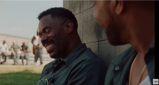 Colman Domingo as a prison inmate sitting against an outdoor courtyard wall, laughing with eyes closed.