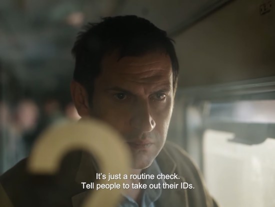 Ordinary train passenger stands at door with yellow number 2 on the glass, concerned at what he's seeing.