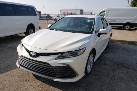 A white 2023 Toyota Camry parked in a dirt parking lot.